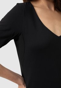 Black V-neck top with three-quarter sleeves, smooth texture, form-fitting design, and a subtle side panel detail.