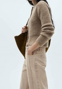 Cárdigan de punto beige con textura acanalada y botones, combinado con pantalones de tiro alto en beige claro. Bolsa tote de ante marrón oscuro.