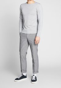 Graues Langarmshirt, graue karierte Slim-Fit-Hose und navyfarbene Sneakers mit weißen Schnürsenkeln, die ein lässiges und dennoch abgestimmtes Outfit zeigen.