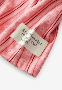 Rosa Stoff mit einem gestreiften Muster und floralen Druckmotiven; verfügt über ein weißes Etikett mit schwarzem Text, auf dem steht: "Sieh das Wunder in den kleinen Dingen."