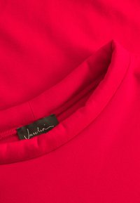 T-shirt aderente a girocollo di un brillante colore rosa, realizzata in tessuto morbido. Presenta un'etichetta con "Vaschio" in scrittura corsiva sul collo sul retro.