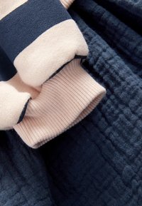 Manche rayée bleu marine et beige avec poignet côtelé reposant sur un tissu bleu foncé texturé.