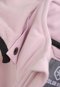 Giacca in fleece rosa chiaro con fodera interna texturizzata, dettagli neri, chiusura a pressione e zip visibile. Design in materiale morbido.