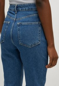 Jeans de mezclilla azul de cintura alta con una textura ligeramente desgastada. Presenta dos bolsillos traseros y una cinturilla visible.
