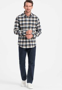 Camicia a quadri in navy, azzurro chiaro e beige, con colletto a punte e maniche lunghe, abbinata a pantaloni in denim scuri e sneaker bianche.