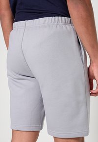 Pantaloncini grigio chiaro con vita elastica, vestibilità affusolata e tessuto morbido e strutturato con orlo pulito sul fondo.