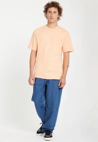 Ferskenfarvet bomulds T-shirt med korte ærmer, rund hals, parret med løstsiddende blå denim jeans og sorte sneakers. Simpelt design, ingen mønstre.
