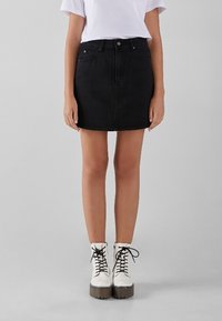 Black denim mini skirt with a front button closure, five-pocket design, and subtle stitching details, paired with white lace-up boots.
