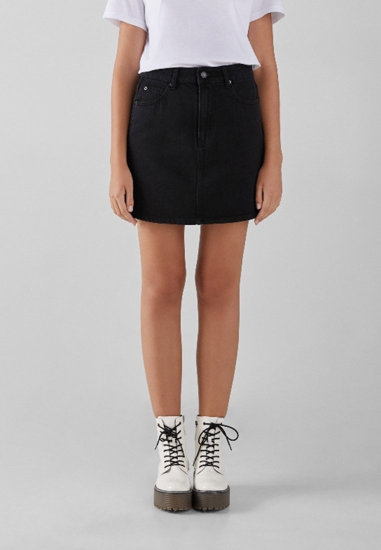 Black denim mini skirt with a front button closure, five-pocket design, and subtle stitching details, paired with white lace-up boots.
