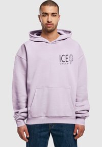 Lila, oversized kapucnis pulóver elülső zsebbel, popsicle grafikával és fekete "FAGYI" felirattal. Pamut anyag.