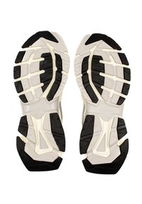 Weiße Sportschuhsohlen mit schwarzen Gummiprofilen, die eine strukturierte Oberfläche und ausgeprägte Rillen für Traktion und Unterstützung aufweisen.