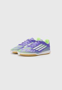 Zapatillas deportivas moradas con detalles en verde, un patrón texturizado y rayas blancas. Suela de goma diseñada para uso en deportes de interior.