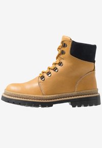 Stivaletti alla caviglia in pelle color cuoio con collo in tessuto nero, occhielli in metallo e suola robusta in gomma nera. Presentano cuciture visibili e superficie strutturata.