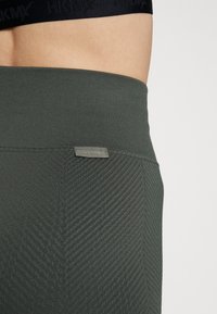 Ciemnozielone legginsy sportowe z teksturowanym wzorem i płaskim pasem, z małą srebrną metką z logo Calvin Klein.