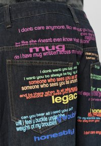 Σκούρα τζιν παντελόνια με πολλαπλές πολύχρωμες φράσεις σε ροζ, πράσινο, κίτρινο και μπλε χρώμα πάνω στις τσέπες και τους μηρούς.