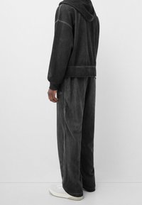 Sudadera con capucha y pantalones deportivos a juego de velour gris oscuro, con un ajuste relajado, bolsillos laterales y una textura suave. Completado con zapatillas blancas.