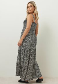 Svart och vit mönstrad maxi-klänning med en smockad överdel, tunna remmar och en flerlagerskjol, tillverkad av lätt tyg.