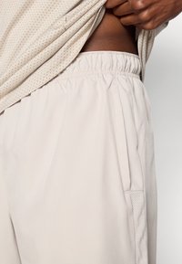 Αθλητικά σορτσάκια σε ανοιχτό μπεζ χρώμα με ελαστική μέση, πλευρικές τσέπες και πλέγμα στις πλαϊνές πλευρές. Απαλή υφή σε όλη την επιφάνεια.