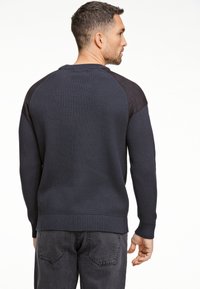 Dunkelblauer, gerippter Pullover mit texturiertem Oberteil und kontrastierenden schwarzen Stoffakzenten an den Schultern. Lange Ärmel und runder Ausschnitt.