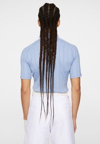 Polo shirt a righe blu chiaro con maniche corte, abbinato a pantaloni bianchi. Lunghi capelli intrecciati cadono lungo la schiena.