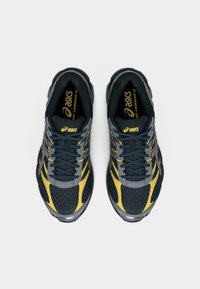 Ζευγάρι μαύρα και κίτρινα παπούτσια τρεξίματος ASICS Gel-Cumulus 16, φωτογραφημένα από πάνω σε απλό λευκό φόντο.