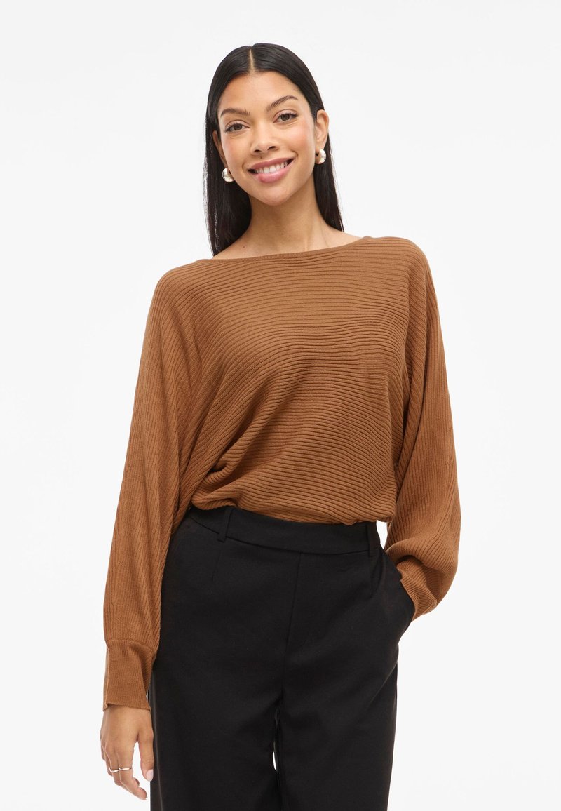 Brown ribbed long-sleeve top with a wide neckline, paired with black pants. The fabric has a soft texture and a relaxed fit.