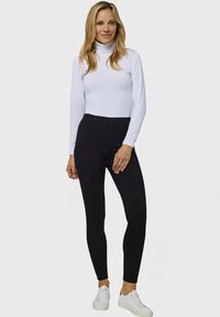 Camiseta de cuello alto blanca con mangas largas, combinada con leggings negros de cintura alta y zapatillas blancas. Textura suave y diseño ajustado.