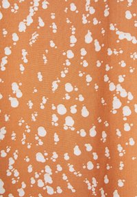 Materiał o pomarańczowym tle, na którym znajdują się różne białe nieregularne kropki w różnych rozmiarach, tworzące teksturowany, zabawny wzór.