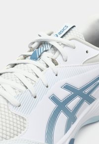Κοντινή λήψη λευκού και μπλε αθλητικού παπουτσιού Asics, εστιασμένη στα κορδόνια, το πλεκτό πάνω μέρος και το λογότυπο στην πλευρά.