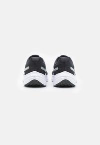 Chaussures de sport noires avec une tige texturée, ornées d'accents gris et d'une semelle blanche. Le design est épuré avec un bout arrondi et une légère élévation.