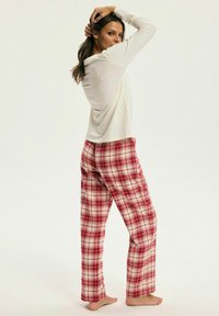 Biała bluzka z długim rękawem zestawiona z czerwonymi, kraciastymi spodnimi od piżamy o wzorze kratki. Miękki materiał, luźny krój i długość do kostek.
