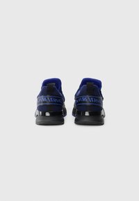 Plave mrežaste tenisice s crnim detaljima, s sjajnom crnom petom i trakicom s logom "Couture Versace" koja se proteže preko pete.