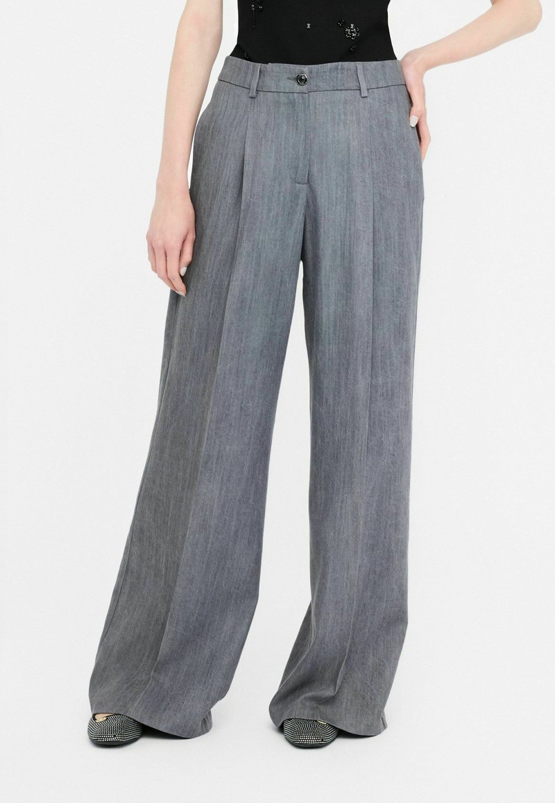 Gray wide-leg trousers featuring a textured fabric, front pleats, and a button closure. Paired with shoes that have a patterned design.