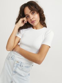 Weißes geripptes T-Shirt mit kurzen Ärmeln, kombiniert mit hellblauen Jeans. Das Oberteil hat einen Rundhalsausschnitt; die Jeans verfügen über ein klassisches Fünf-Taschen-Design.