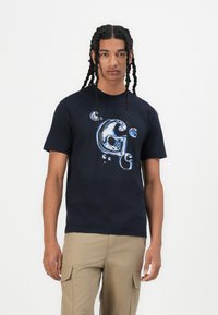 Navy katoenen t-shirt met een glanzend blauw graphic ontwerp dat lijkt op de letter 'G' met luchtbellen. Korte mouwen, ronde hals, ontspannen pasvorm.