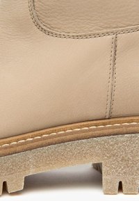 Stivale in pelle beige con texture liscia, suola marrone a contrasto e cuciture visibili lungo i bordi superiori e della suola.