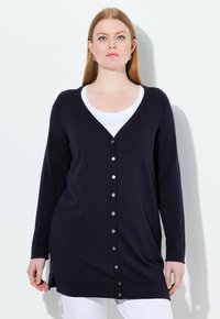 Marinblå långärmad cardigan, lätt stickad tyg, v-ringning, knäppning framtill, sidslitsar i fållen, ihop med en vit topp under.