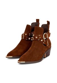 Stivaletti in suede marrone con punta affusolata, caratterizzati da accessori in metallo dorato, dettagli con borchie e un design a tacco impilato.