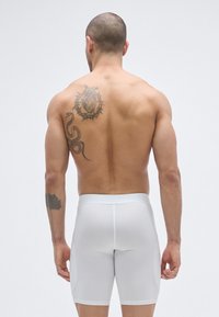Λευκά σ ορτς με ραφή, κατασκευασμένα από ελαστικό ύφασμα, με στενή γραμμή, ομαλή υφή και λογότυπο στη μέση. Διαθέτουν πλαϊνές τσέπες.