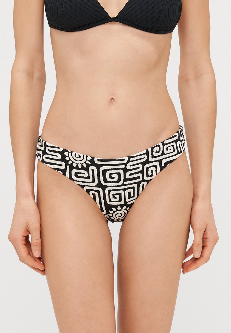 Μαύρα και λευκά σλιπ μπικίνι με υφή, που διαθέτουν γεωμετρικά σχέδια και αφηρημένα σχέδια. Χαμηλή μέση με πλαϊνές ανοίξεις.