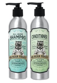 Bottiglie metalliche con erogatori a pompa per shampoo e balsamo. Etichette verde e beige con un orso in salopette, con dettagli dell'etichetta ben visibili.