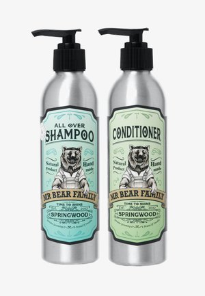 Bottiglie metalliche con erogatori a pompa per shampoo e balsamo. Etichette verde e beige con un orso in salopette, con dettagli dell'etichetta ben visibili.