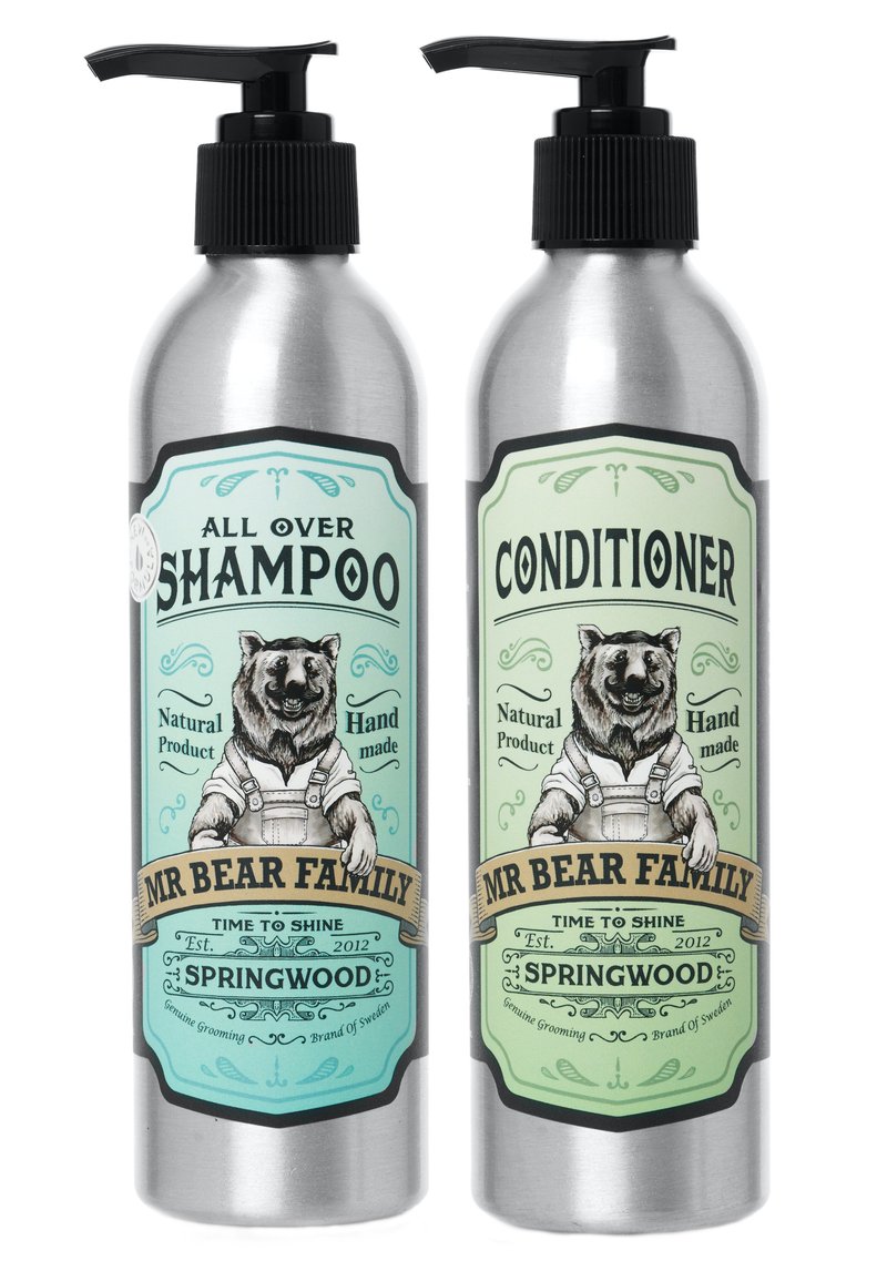 Bottiglie metalliche con erogatori a pompa per shampoo e balsamo. Etichette verde e beige con un orso in salopette, con dettagli dell'etichetta ben visibili.