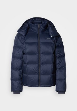 Marineblauer Steppjacke aus glänzendem, wattiertem Material. Verfügt über einen hohen Kragen, einen durchgehenden Reißverschluss und enge Bündchen für Wärme. Logo auf der Brust.