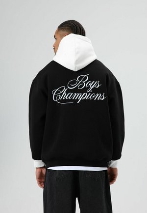 Zwarte oversized hoodie met een witte capuchon. Voorzien van grote witte cursieve tekst "Boys Champions" op de achterkant. Gemaakt van een katoenmengsel, met een losse pasvorm.