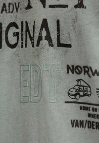 Close-up of gray fabric with black and outlined text, including "ORIGINAL," "EDIT," and a small drawing of a van with "NORW" text.