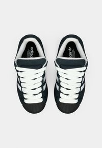 Black and navy suede sneakers with a rubber shell toe, featuring white laces and three white stripes on each side.