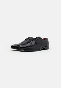 Scarpe eleganti da uomo in pelle nera con finitura lucida, punta tonda e design con lacci. Presentano una suola testurizzata e dettagli interni rossi.