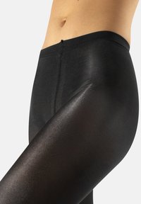 Leggings neri con una texture liscia e lucida, vita alta e un design aderente, che mettono in mostra un aspetto senza cuciture sulla coscia.