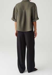 Chemise à manches courtes vert olive avec un motif côtelé texturé ; coupe décontractée. Associée à un pantalon large noir en tissu lisse, sandales à talon empilé.